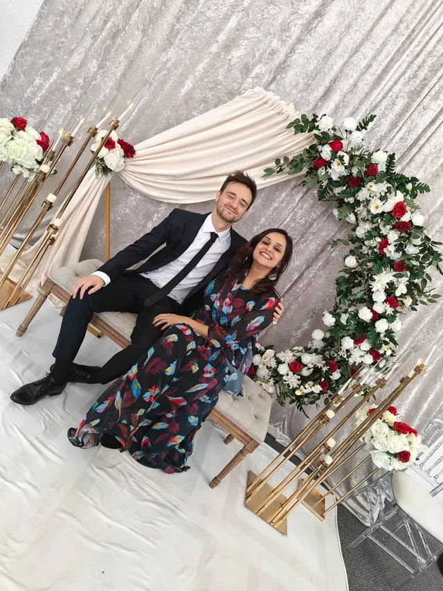 Krishna and Matt seated on a stage decorated with white and red flowers and gold candles