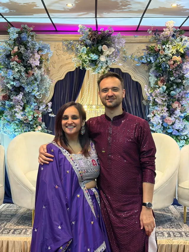 Krishna and Matt in front of a reception stage dressed with blue and lilac flowers